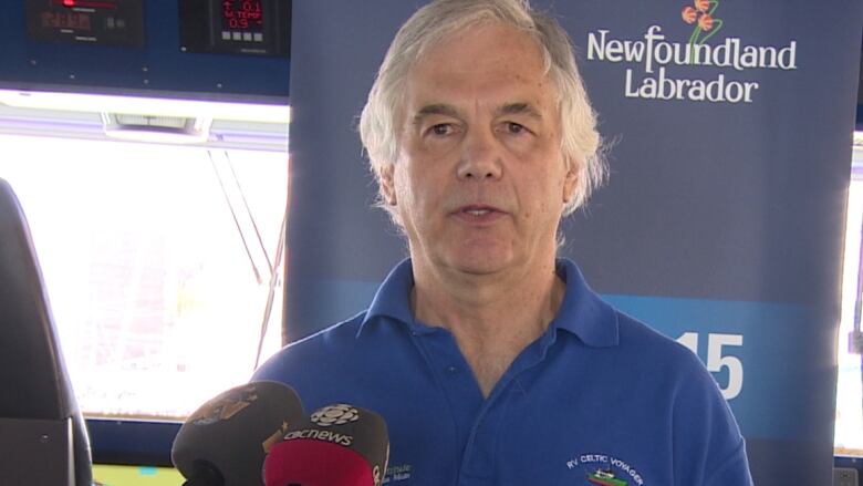 Man with grey hair stands in front of three microphones.