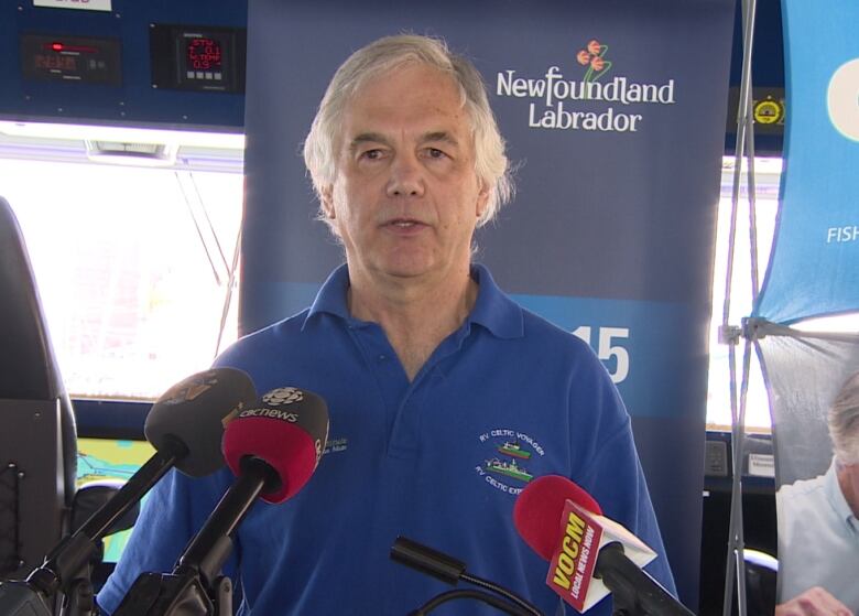 Man with grey hair stands in front of three microphones.