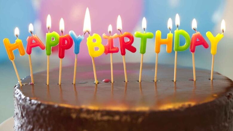 A chocolate birthday cake with lit candles that spell out, 'HAPPY BIRTHDAY.'