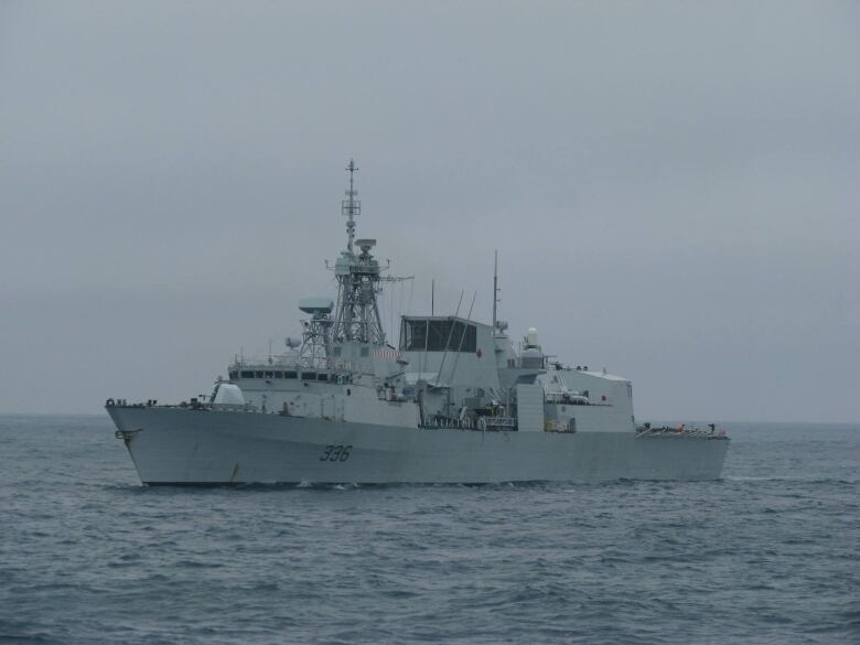 A large grey Canadian warship floats alone in open water, with no land in sight.