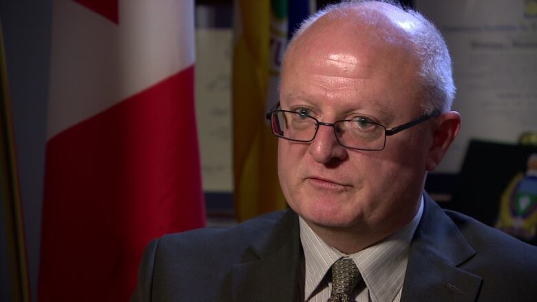 A man wearing black-framed glasses and a suit speaks.