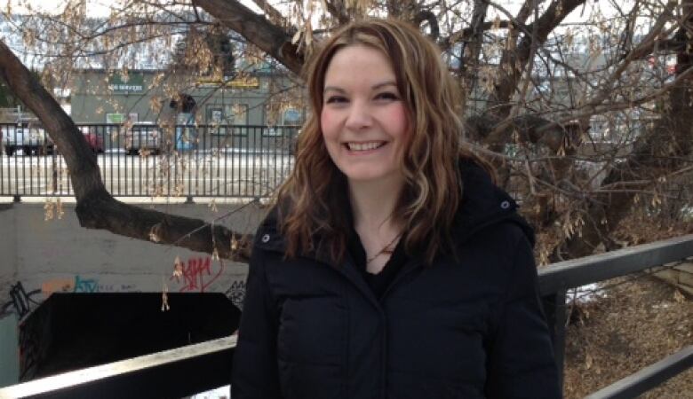 A woman with wavy, light brown hair and highlights, dressed in a black puffer jacket smiles at the camera.