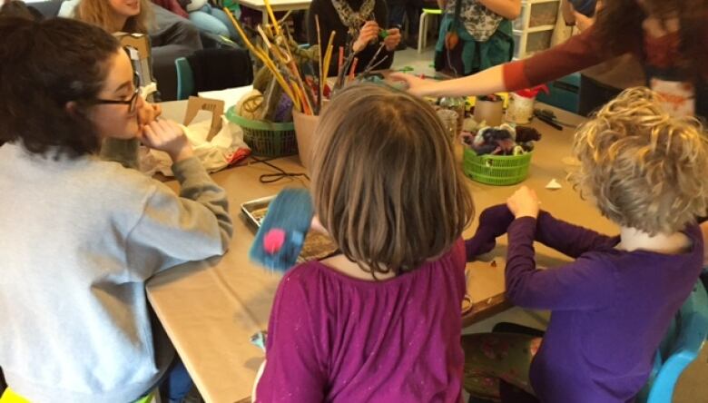 Children with their backs to the camera use various art supplies on a table