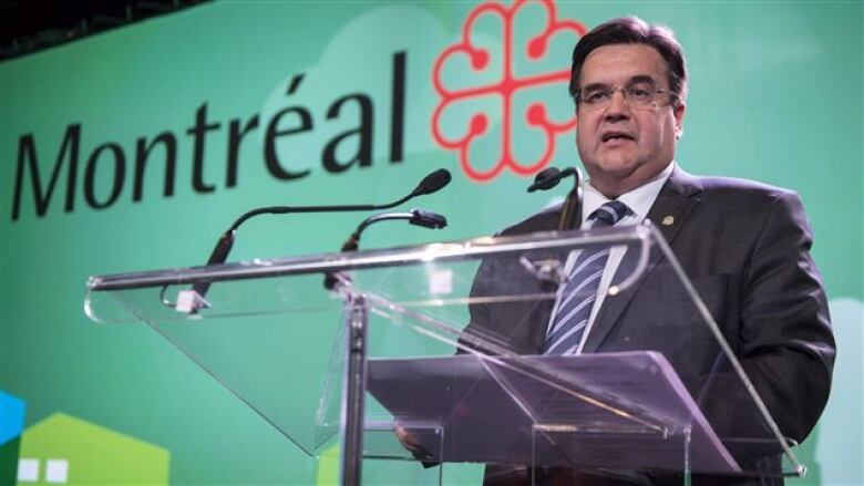 A man stands and speaks from behind a glass podium.