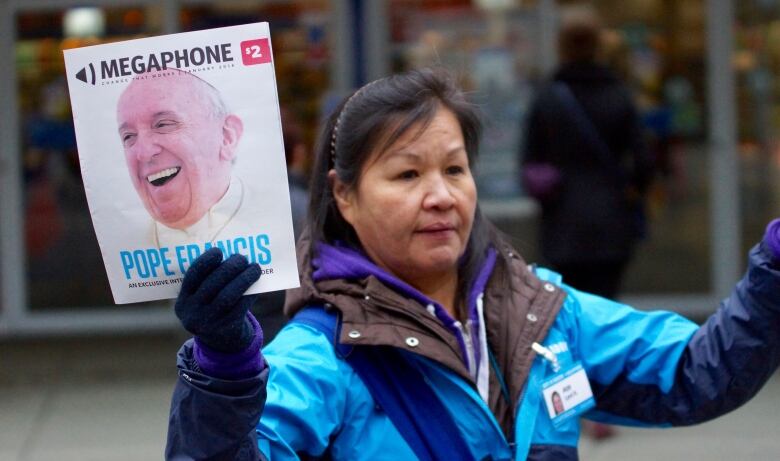 A woman holding a Megaphone magazine out in the streets. 