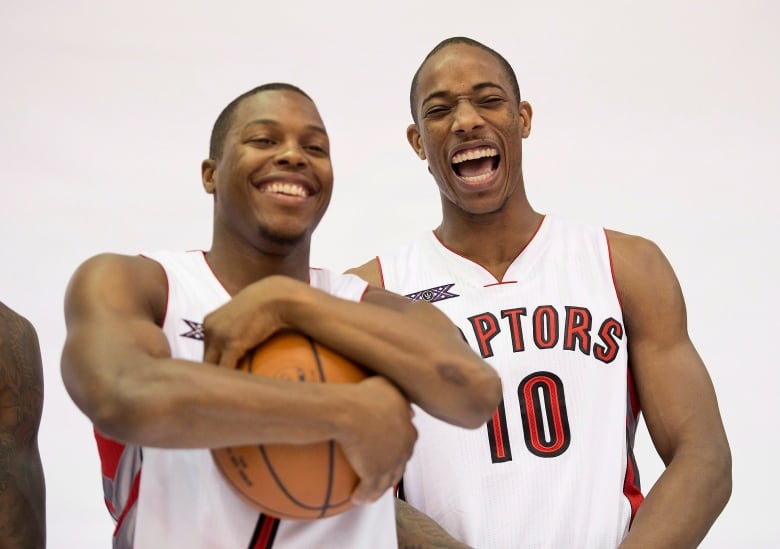 One man holds a ball while the other flexes at the camera.