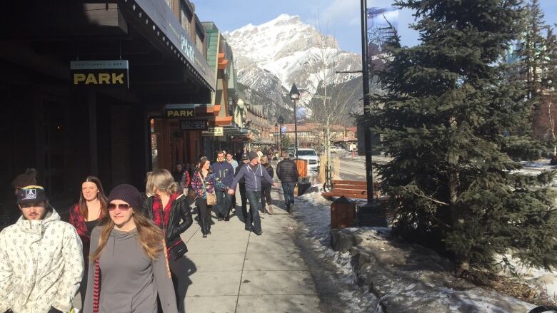 Tourists walk along a busy sidewalk in a mountain town.