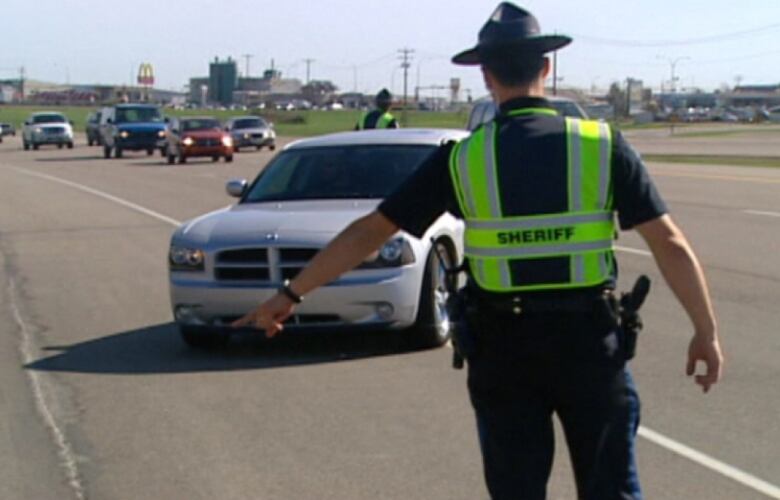 A person wearing a sheriff's jacket directs a car to pull to the side of the road.