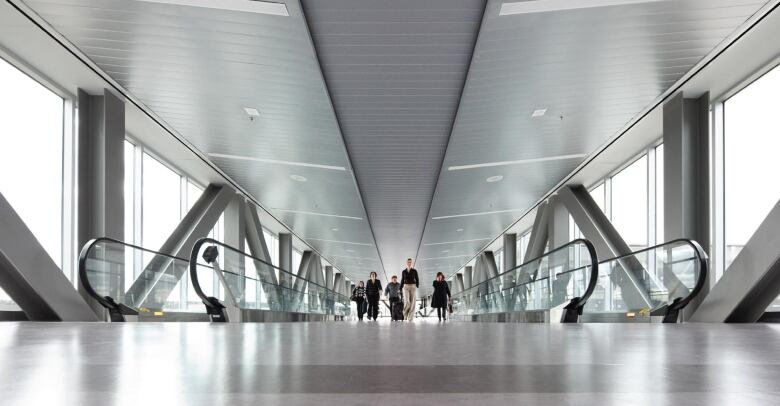 People walk along a grey metal moving walkway at an airport