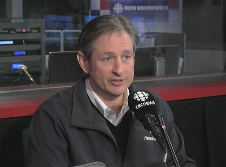 A man wearing a black jacket speaks into a CBC microphone during an interview. 