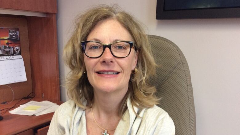 Woman in glasses smiles as she sits at a desk.