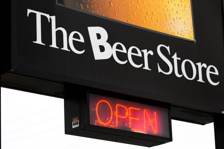 A large sign outdoors on a cloudy day, close up, reads The Beer Store in white text against a black background, with a red neon 