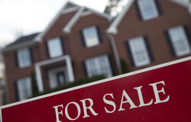 A red for-sale sign in front of a red brick home.