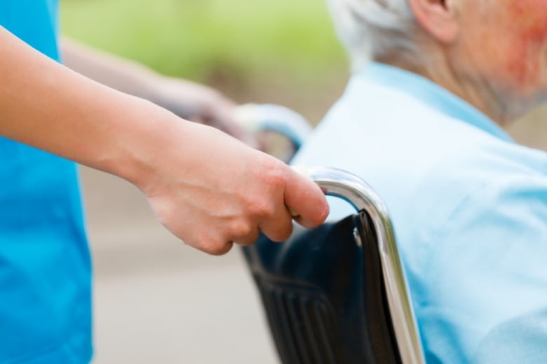 Close up image of a nurse pushing an elderly person in a wheelchair.