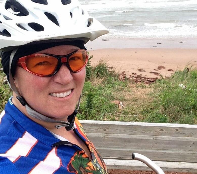 A woman wearing a bike helmet on a path in front of the ocean. 