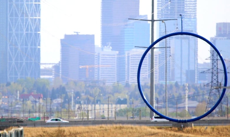 A giant blue ring with what looks like a street lamp on top sits on a road as the Calgary skyline looms in the background.