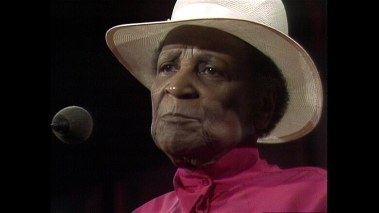 A Black woman wearing a beige hat and a red top