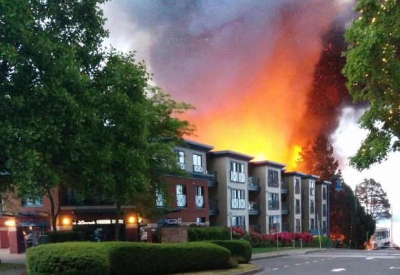 Red flames shooting from the roof of an apartment complex light up the night sky.