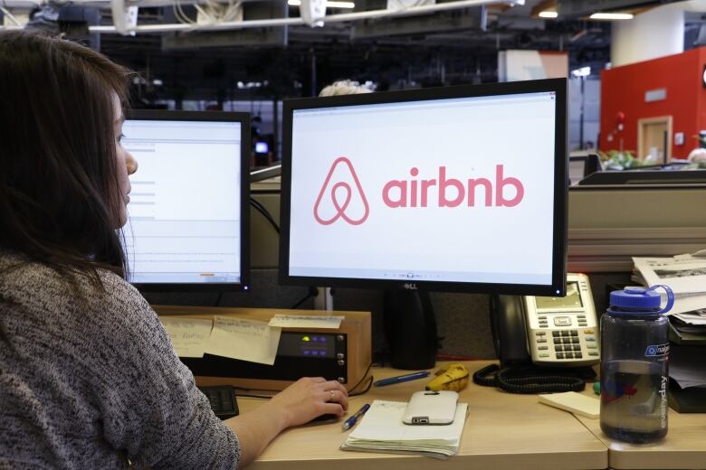 A woman looks at a computer screen with Airbnb logo on it.