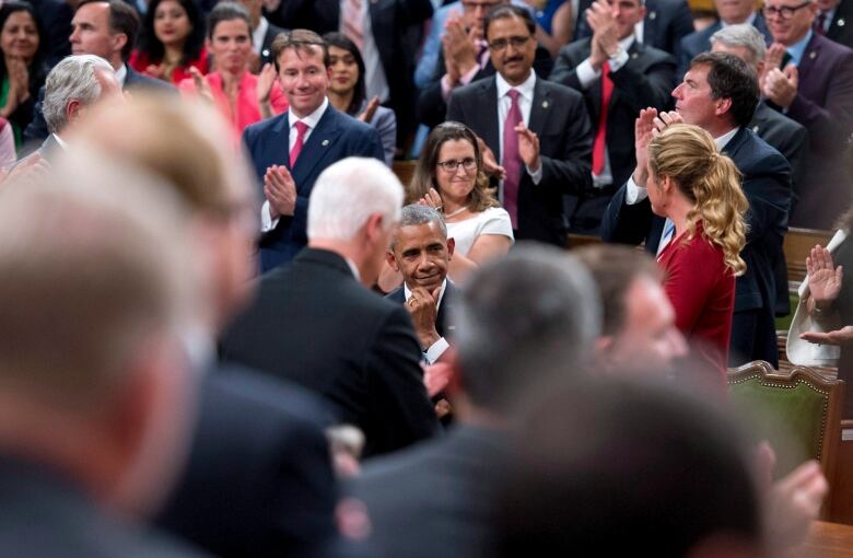 Barack Obama smiles while being applauded by a crowd of people.