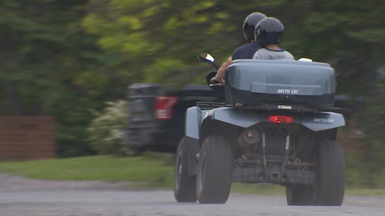 An off-road vehicle is shown from behind, moving, with two people on it, one behind the other.