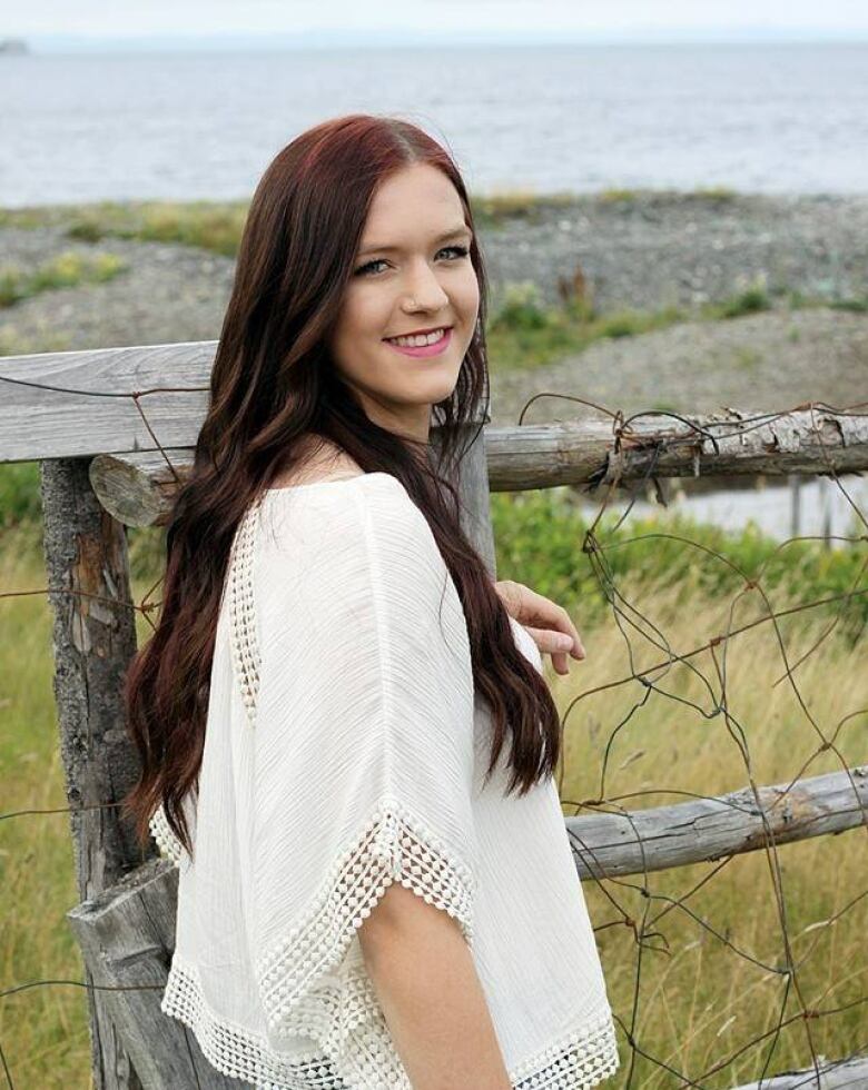 woman standing next to a fence and the ocean.