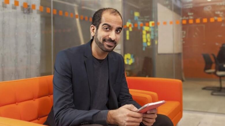 A man sits on an orange couch in an office.