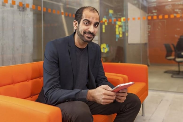 A man sits on an orange couch in an office.