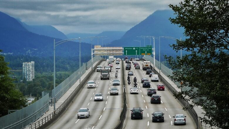 Rows of cars and bikes cross a bridge leading into the mountains.