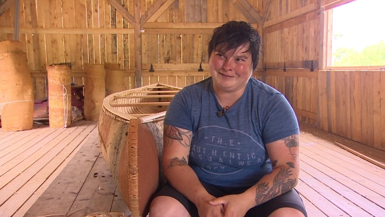 a woman sits in front of a birch bark canoe. 