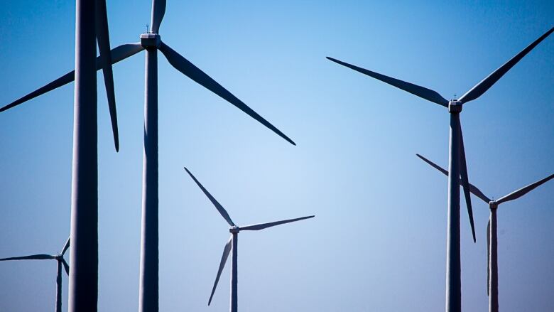 Six wind turbines are seen against the backdrop of a clear blue sky. 