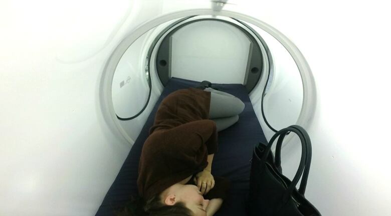 A person sleeps on their side within a white cylindrical sleeping pod.