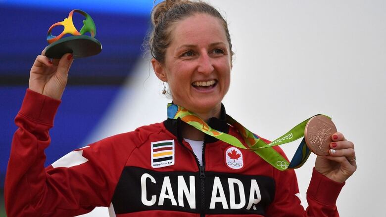 A woman in a Canada zip-up sweater celebrates with a bronze medal