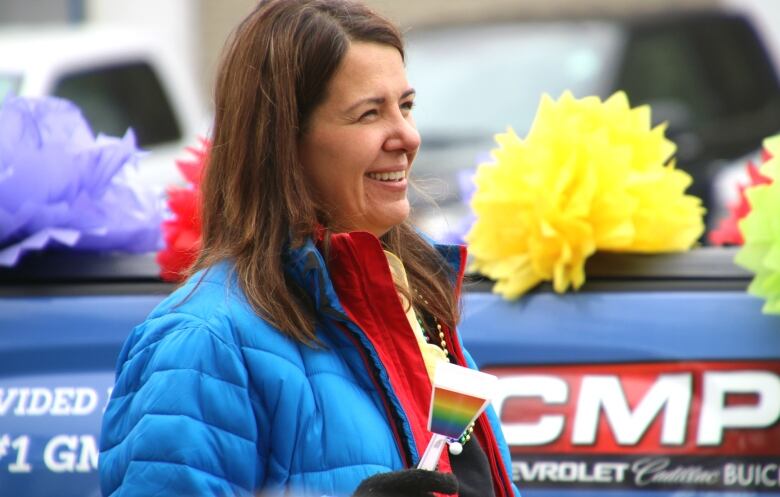 woman holds a rainbow noisemaker behind a car dealership's Pride parade float