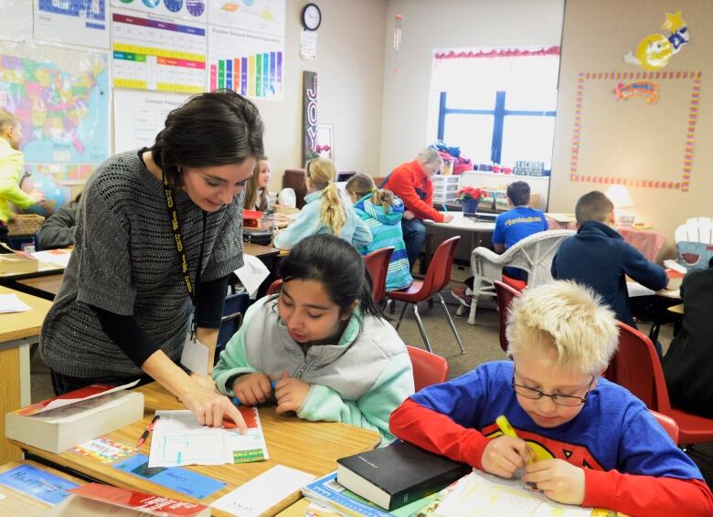 Teacher stands over small group of students in classroom.