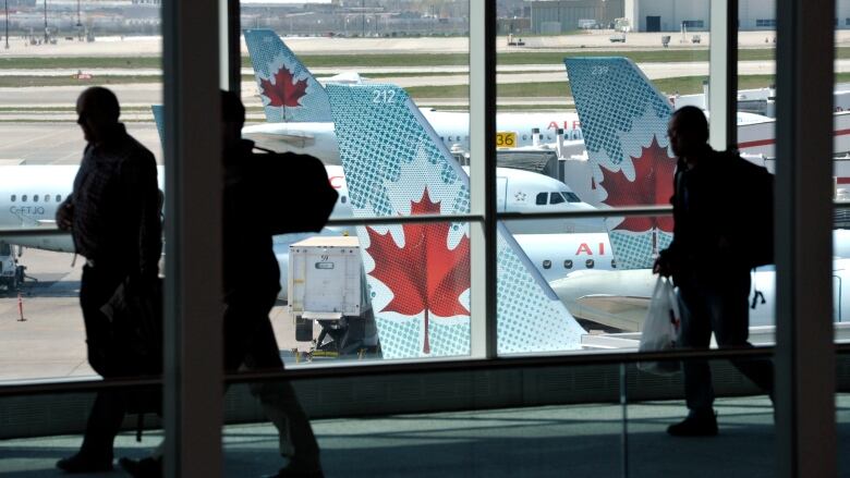 Passengers walk in an airport in front of a window. Outside, there are planes.