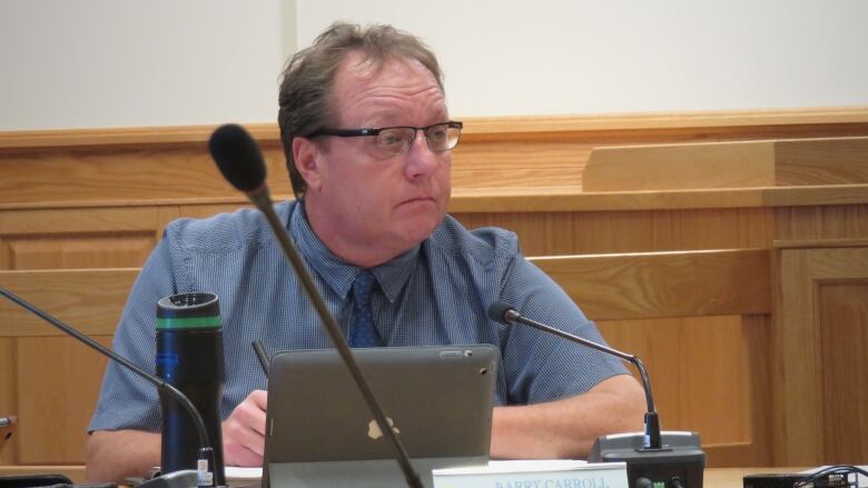 A white man sits in a council chamber.