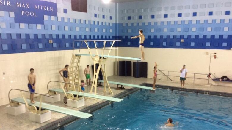 A pool with four diving boards and people swimming