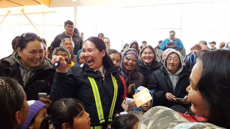 A woman smiles, holding a pin. She is surrounded by people and is holding a card. 