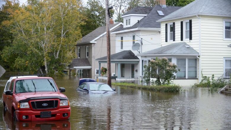 Vehicles are seen submerged in water on a flooded residential street.