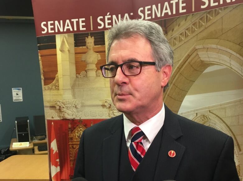 A man with glasses wearing a suit and tie is seen standing in front of a microphone.