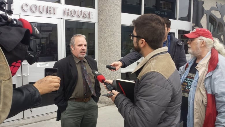 A man stands outside a building labelled Court House, being scrummed by reporters.