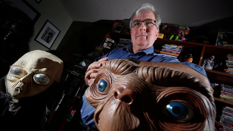 A man stands in front of two figurines of aliens.