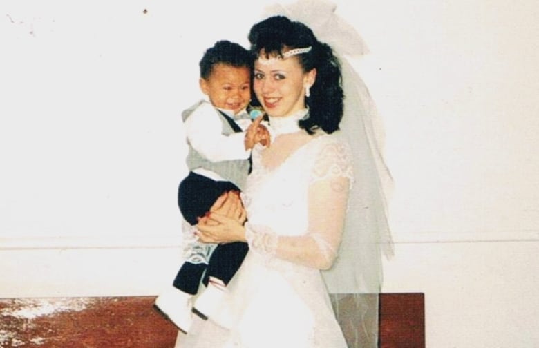 A woman in a wedding gown, holding a little boy.