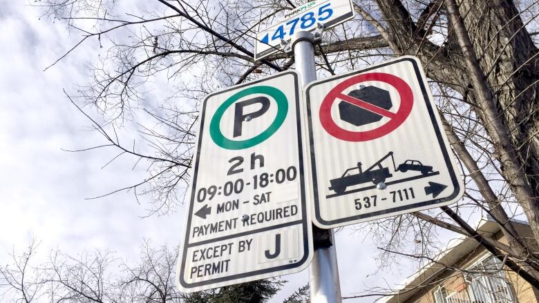 Street signs indicating parking rules are seen in a photograph against a partly cloudy sky.