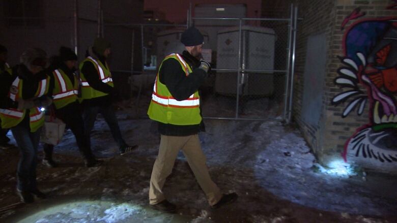 A group of people walk with flashlights on a snowy sidewalk.