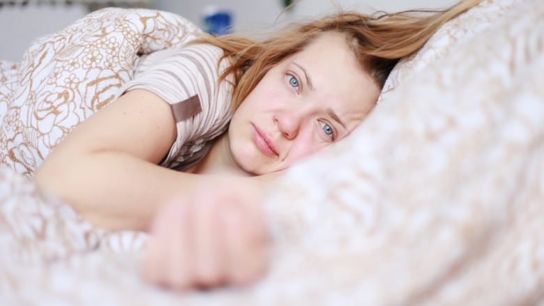 A woman looks sad as she lies on her side in bed.