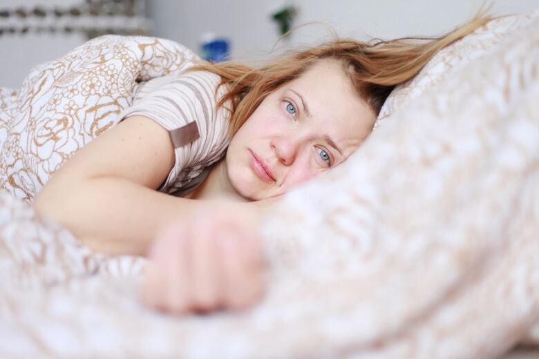 A woman looks sad as she lies on her side in bed.