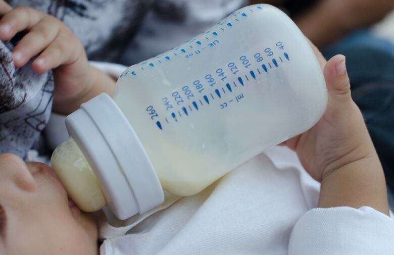 A closeup of a baby drinking formula from a bottle.