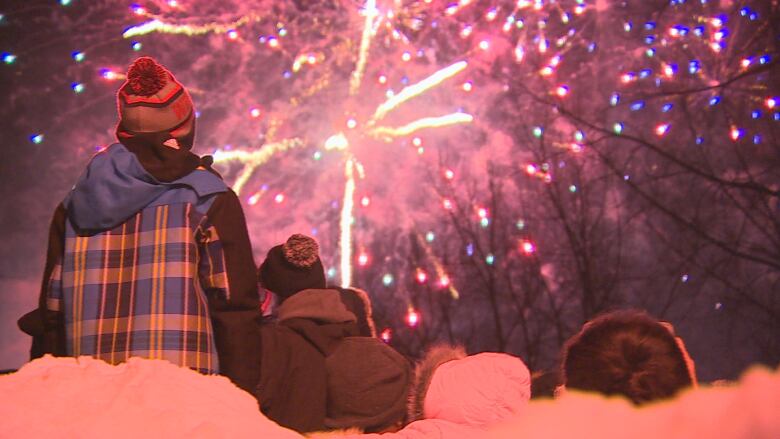 A child sits on an adult's shoulders facing fireworks.